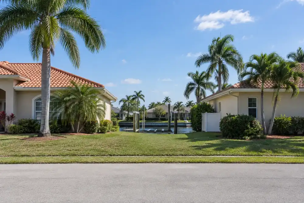 Palm trees line a quiet street of stucco homes beside a glimpse of canal.