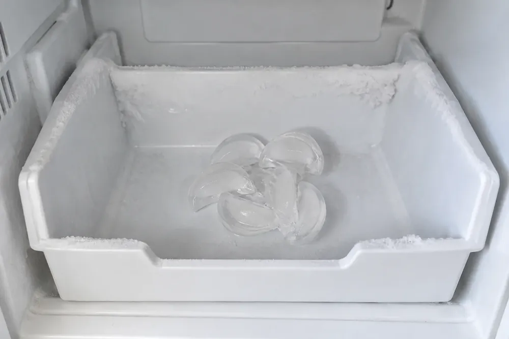 Freezer ice bin with crescent cubes fused together and frost along its edges